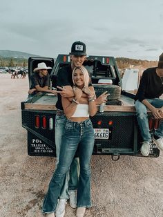 two people sitting on the back of a pick up truck with their arms around each other