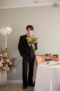 a young man in a tuxedo standing next to a table with a cake and flowers