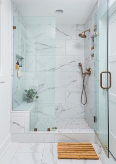 a walk in shower sitting next to a white tiled wall and wooden bench on the floor