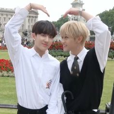 two young men standing next to each other in front of a flower garden and building