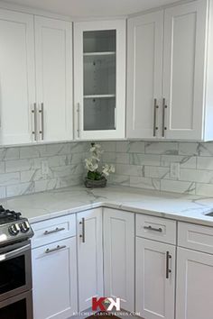 a white kitchen with marble counter tops and stainless steel stove top oven in the corner