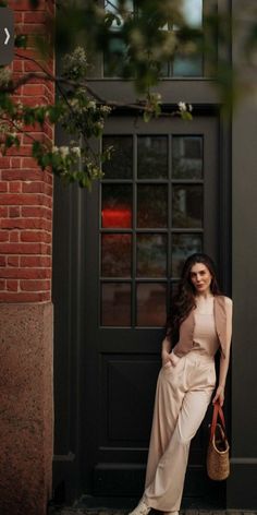 a woman leaning against a door with her hand on her hip and holding a purse