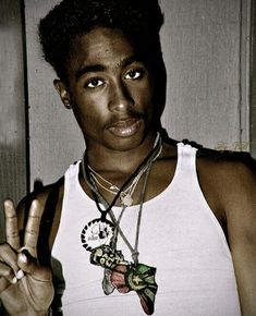 a young man making the peace sign with his hand while wearing a tank top and necklace