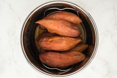 three sweet potatoes in a pot on a marble counter top, ready to be cooked