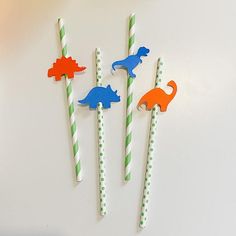 three dinosaur straw toppers on green and white striped paper sticks with orange and blue dino toothbrushes