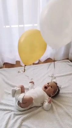 a baby laying on top of a bed next to a yellow balloon