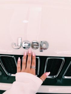 a woman's hand on the front grille of a white car with jeep written on it