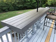 an outdoor deck with bar stools and table on it in the middle of a yard