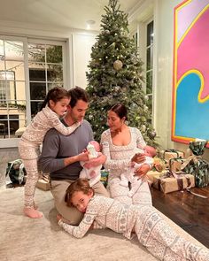 a man and two women are holding their babies in front of a christmas tree