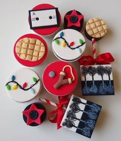 decorated cupcakes and cookies are arranged on a white surface with red ribbon around them