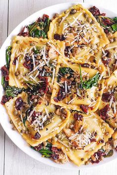 a white bowl filled with pasta and spinach covered in cheese on top of a wooden table