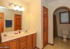 a bathroom with two sinks, a toilet and an archway leading to the other room