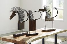 three metal sculptures sitting on top of a wooden table in front of a white wall