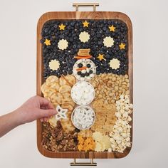 a snowman made out of crackers and cereals on a wooden platter