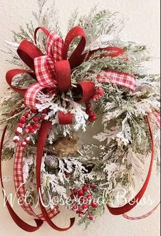 a christmas wreath hanging on the wall with red and white ribbons, pine cones, and berries