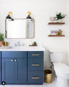 a white toilet sitting next to a blue vanity in a bathroom under a large mirror