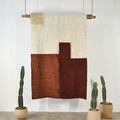 two potted cacti in front of a wall hanging