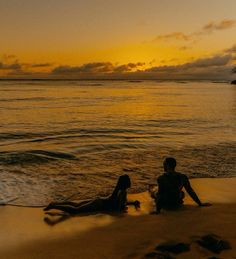 two people are sitting on the beach at sunset