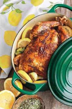 a chicken in a pot with lemons and herbs next to it on a wooden table