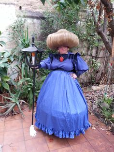 a woman in a blue dress with a large hat on her head is standing next to a lamp post