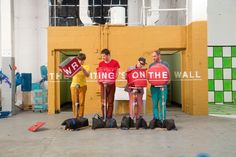 three people standing in front of a building holding signs and wearing red vests with the words, waiting is on the wall