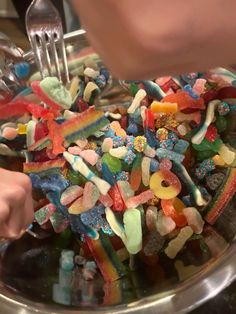 a bowl filled with lots of different colored candies next to a person holding a fork