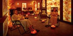 two women are sitting in chairs with candles on the floor and one is wearing a robe