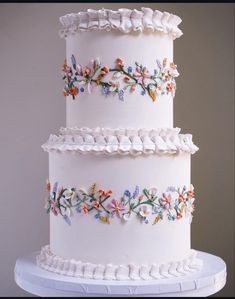 a three tiered white cake with colorful flowers on the side and ruffled edges