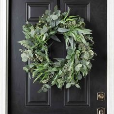 a wreath on the front door of a house with green leaves and greenery hanging from it