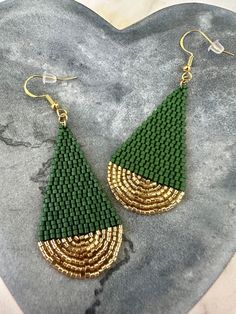 green and gold beaded earrings on top of a heart shaped stone slab with the shape of a triangle in the center