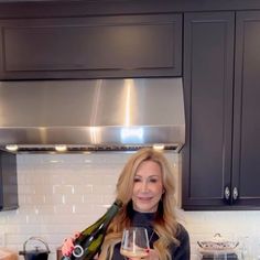 a woman holding a glass of wine in her hand while standing next to a stove