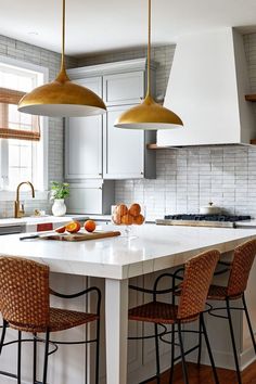 a kitchen with two pendant lights hanging over the island and three bar stools in front of it