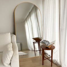 a white couch sitting next to a mirror on top of a wooden table in front of a window