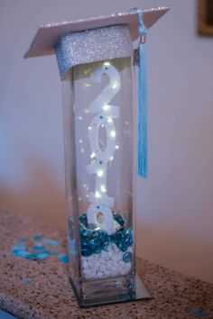 a graduation cap is decorated with lights and streamers in a clear glass container on a table