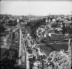 black and white photograph of people walking on the side of a bridge over a river