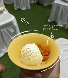 a hand holding a yellow bowl filled with ice cream next to tables covered in white linens