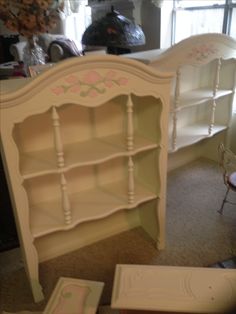 a white bookcase with pink flowers painted on the top and bottom, sitting in front of a window