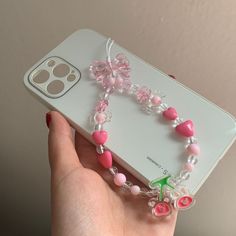 a hand holding a cell phone with a pink and white beaded bracelet attached to it