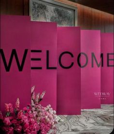 pink paper bags with the word welcome on them are sitting next to flowers and vases