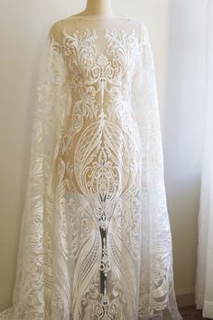 a white lace dress on a mannequin stand in front of a curtained window