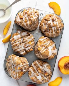 peach muffins with icing on a baking tray next to sliced peaches