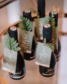 four wine bottles with labels on them are sitting on a glass table and decorated with greenery