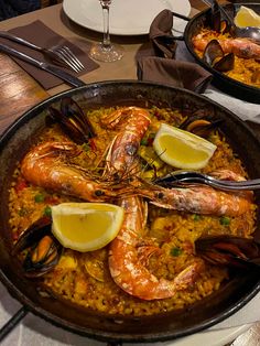 two pans filled with seafood and rice on top of a table next to wine glasses