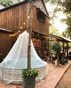 an outdoor hot tub with mosquito netting on it in front of a wooden building surrounded by greenery