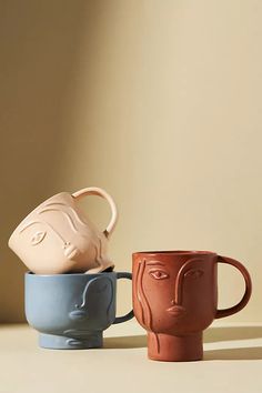 three coffee mugs with faces on them sitting side by side in front of a beige wall