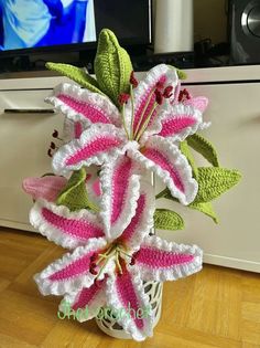 a crocheted flower in a vase on a wooden floor next to a television