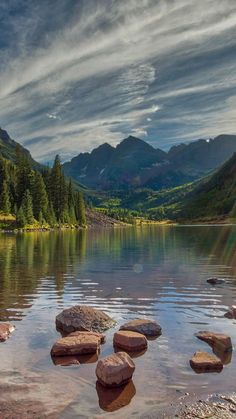 some rocks are in the water near mountains