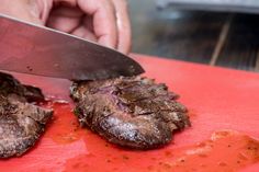 a person is cutting up some meat on a red cutting board with a large knife