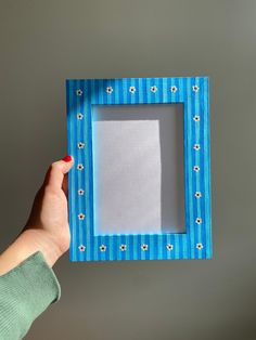 a person holding up a blue frame with white flowers on the bottom and one side