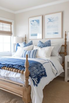 a bed with blue and white pillows in a bedroom next to two pictures on the wall